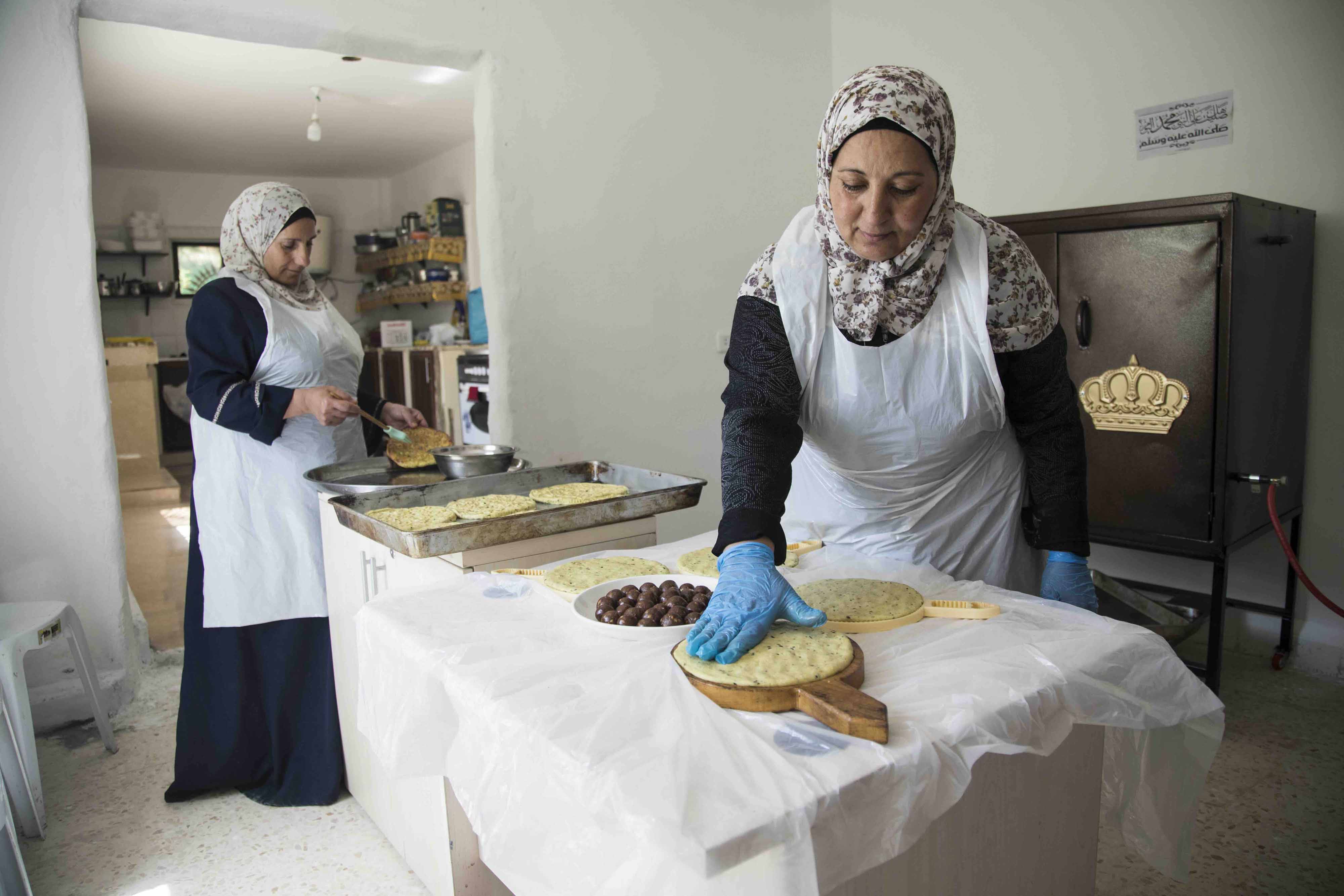 image of two ladies wearing headscarves working in a bakery making bread.