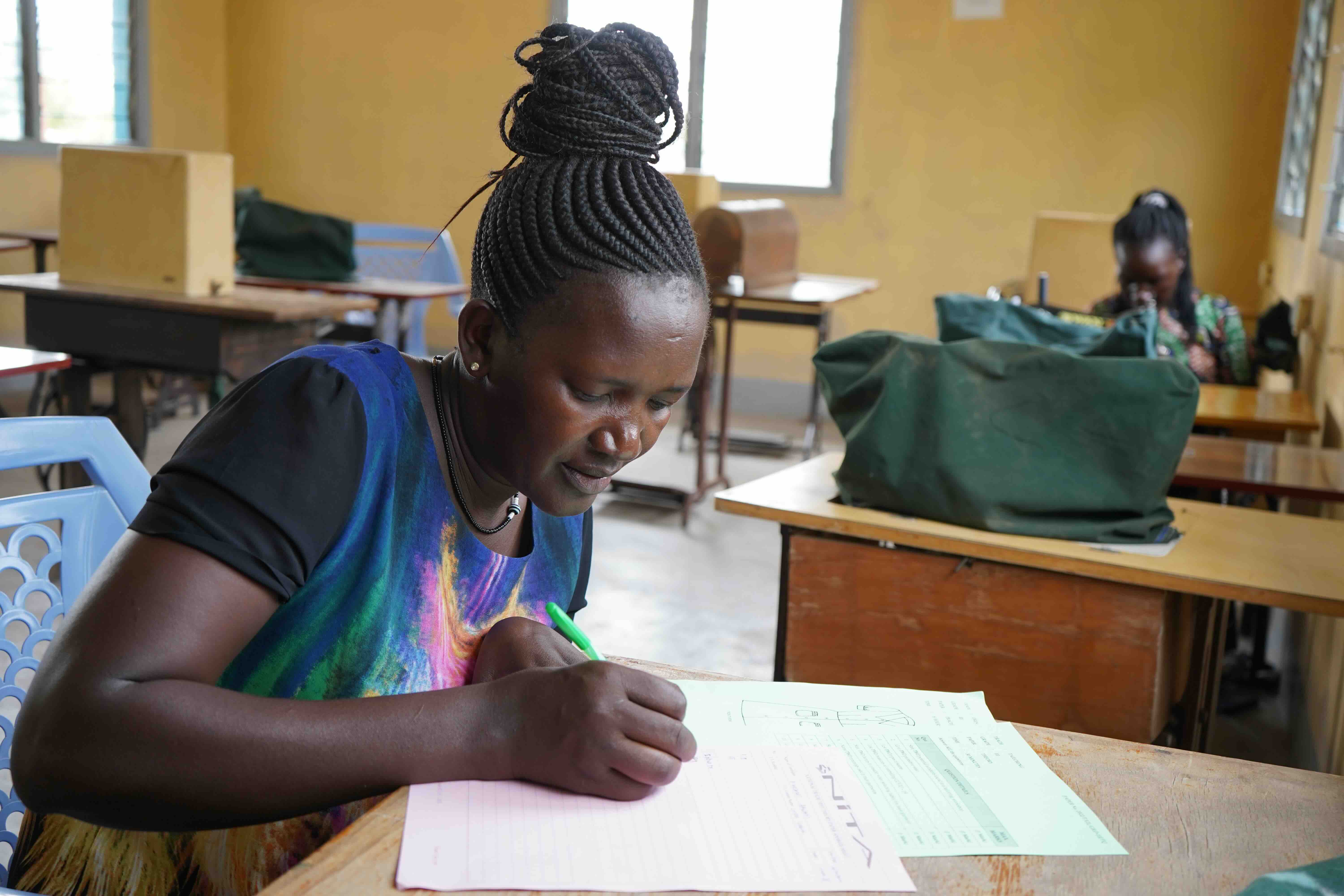 Image of a lady filling out a form in a workshop with sewing machines in the background