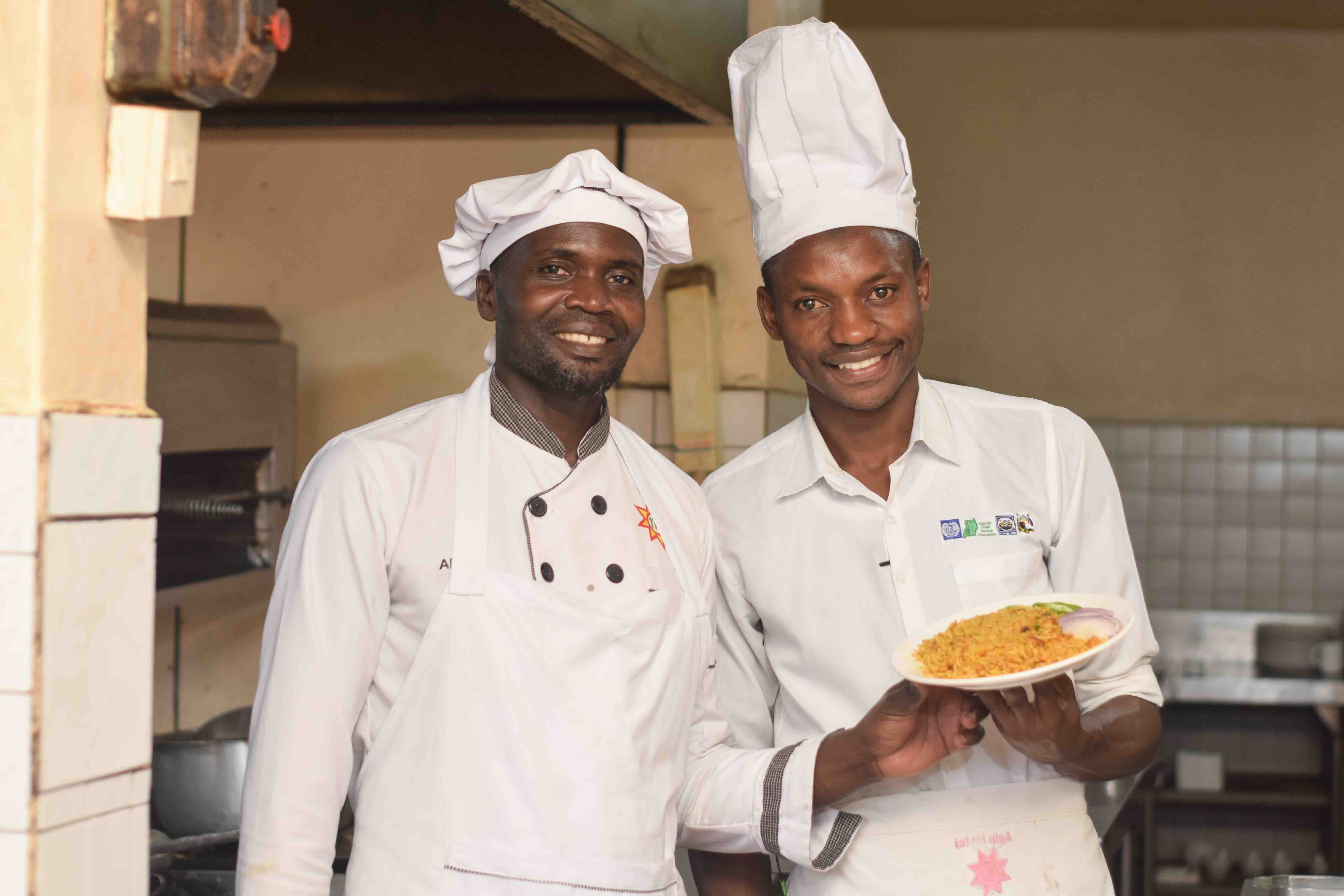 Image of two young person dressed in chef's uniform in a kitchen holding a dish on display